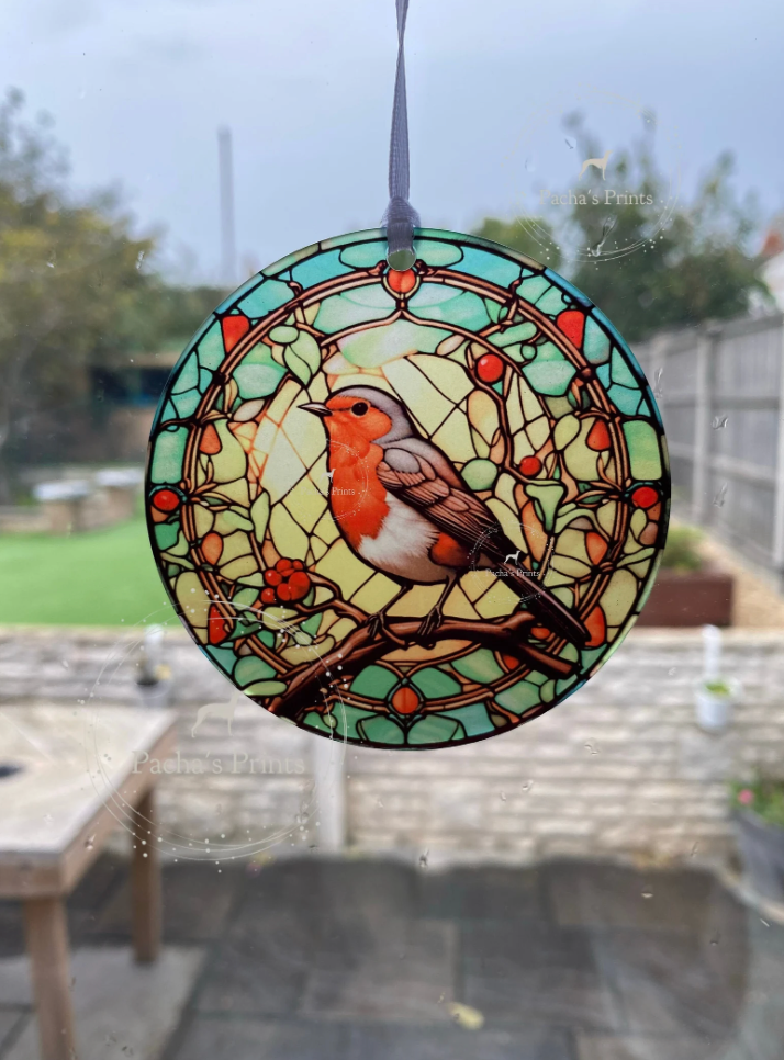 Stained glass window hanging with a robin design, outdoors.