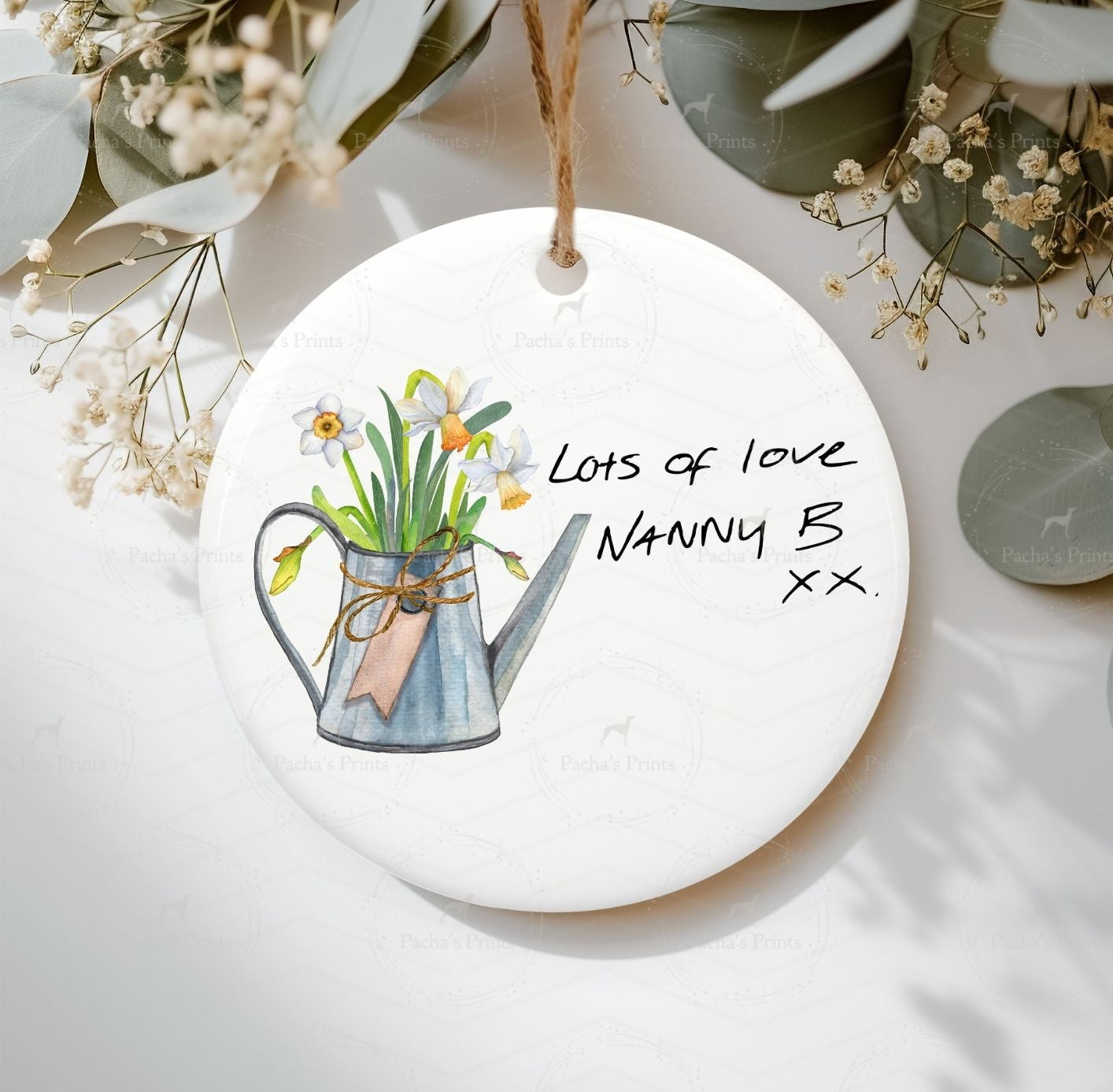 Round ceramic ornament with a watering can and flowers illustration, text 'Lots of love Nanny B xx' on a white background.