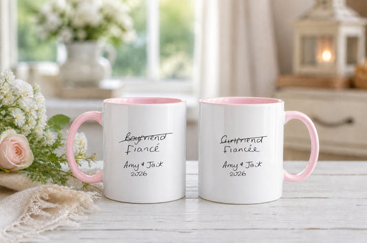 Two white mugs with pink handles on a table with flowers and a blurred background