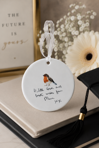 Decorative ornament with a bird illustration and text, placed on a surface with flowers and a book.