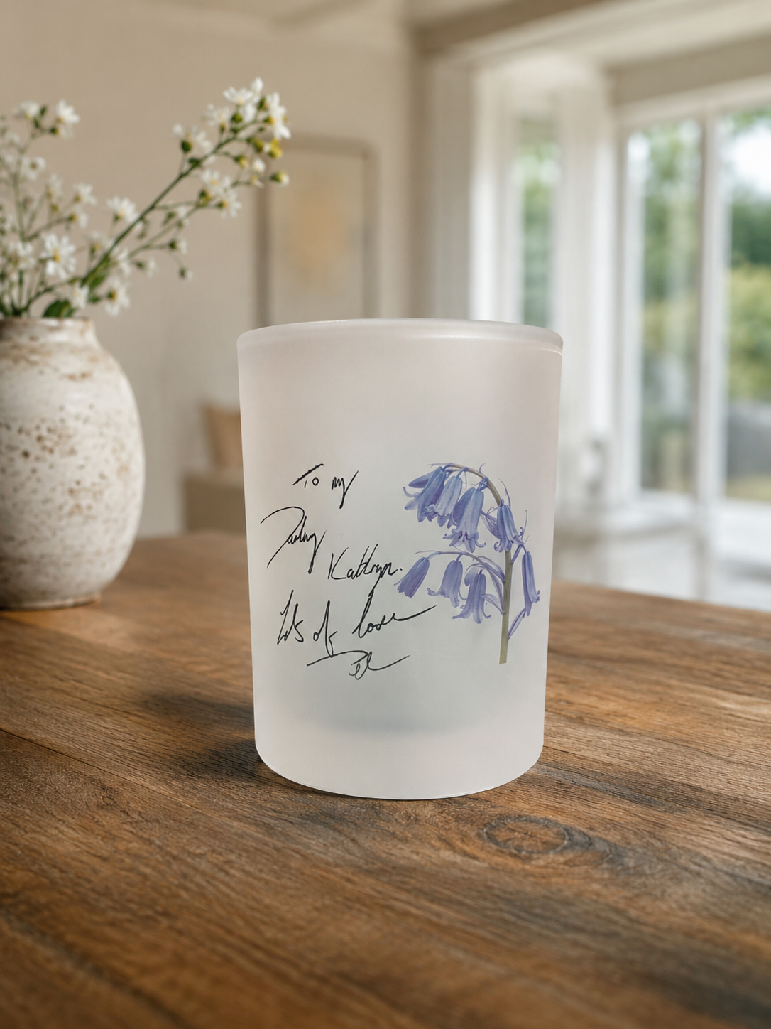 Frosted candle with floral design and text on a wooden surface