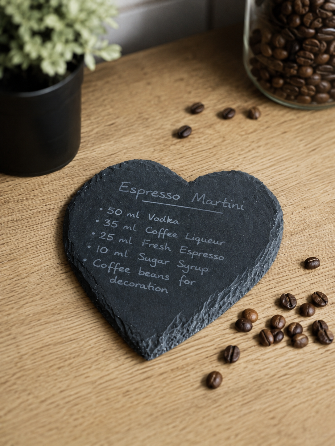 Heart-shaped slate coaster with espresso martini recipe on a wooden surface with coffee beans and a plant.