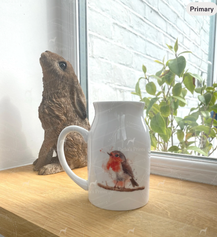 White mug with a bird design on a wooden surface next to a rabbit and plant
