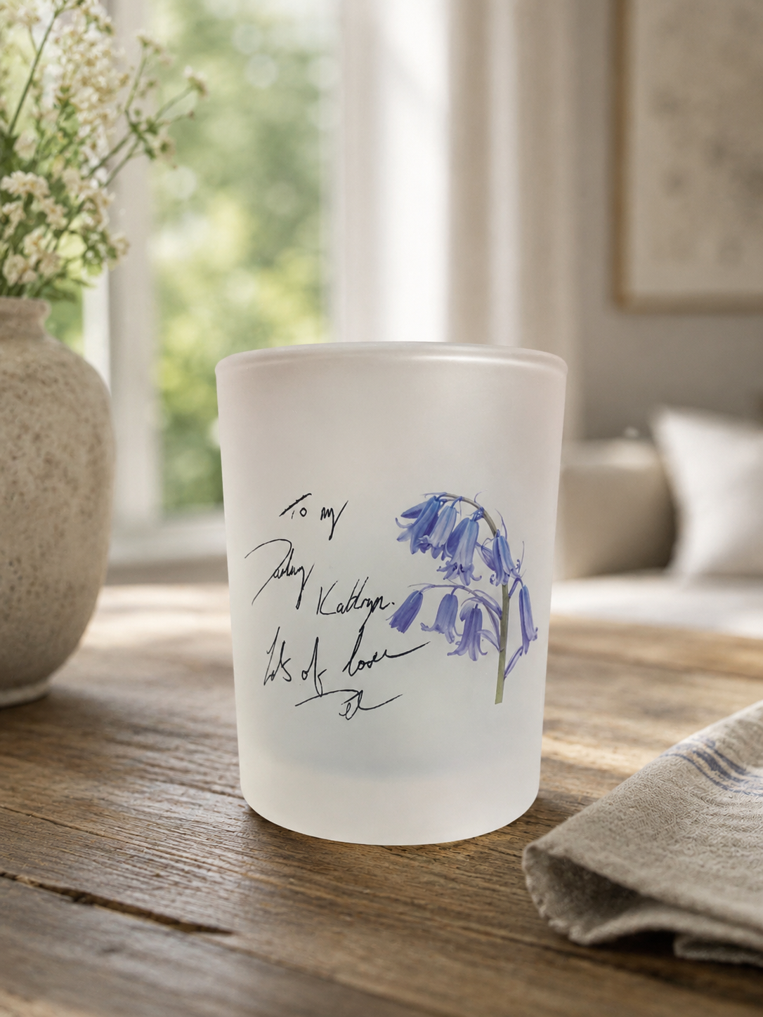 Frosted glass candle with floral design and text on a wooden surface