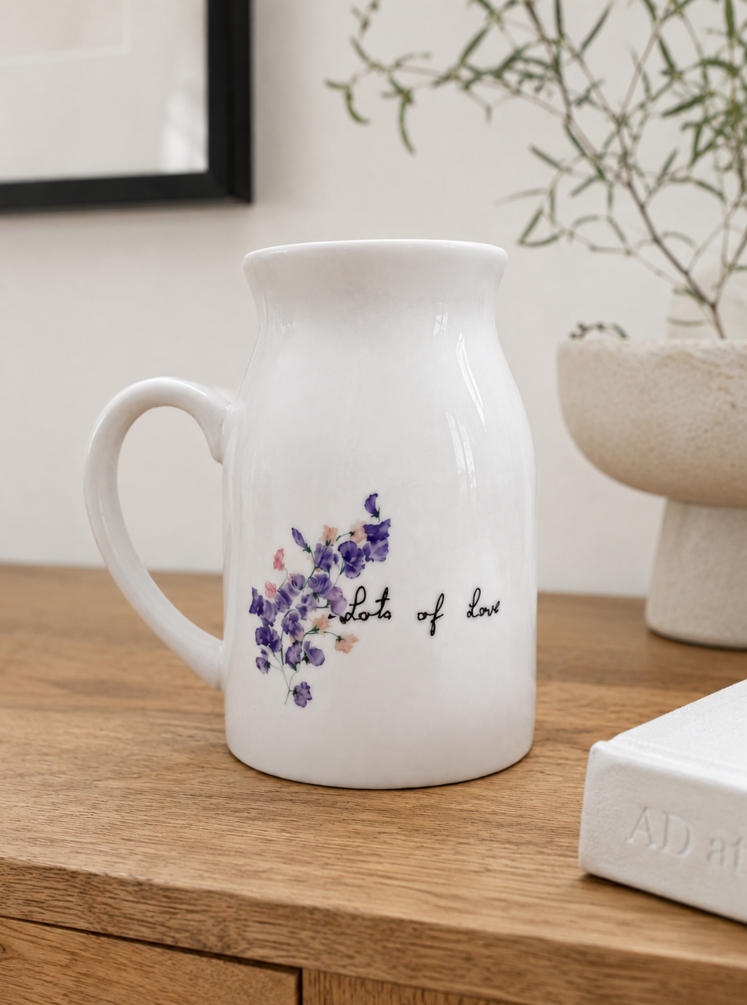 White ceramic pitcher with floral design and text on a wooden surface