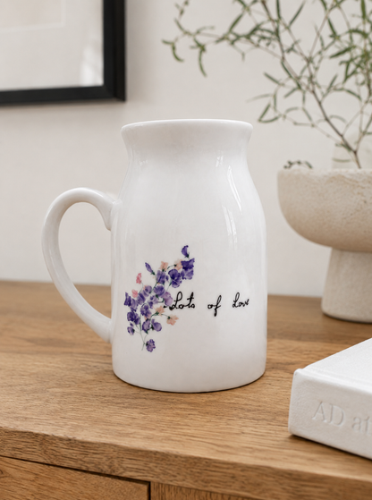 White ceramic pitcher with floral design and text on a wooden surface