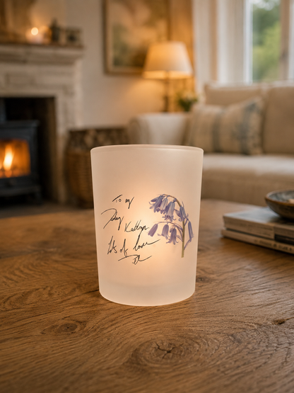 Frosted candle holder with floral design and text on a wooden table in a cozy living room.