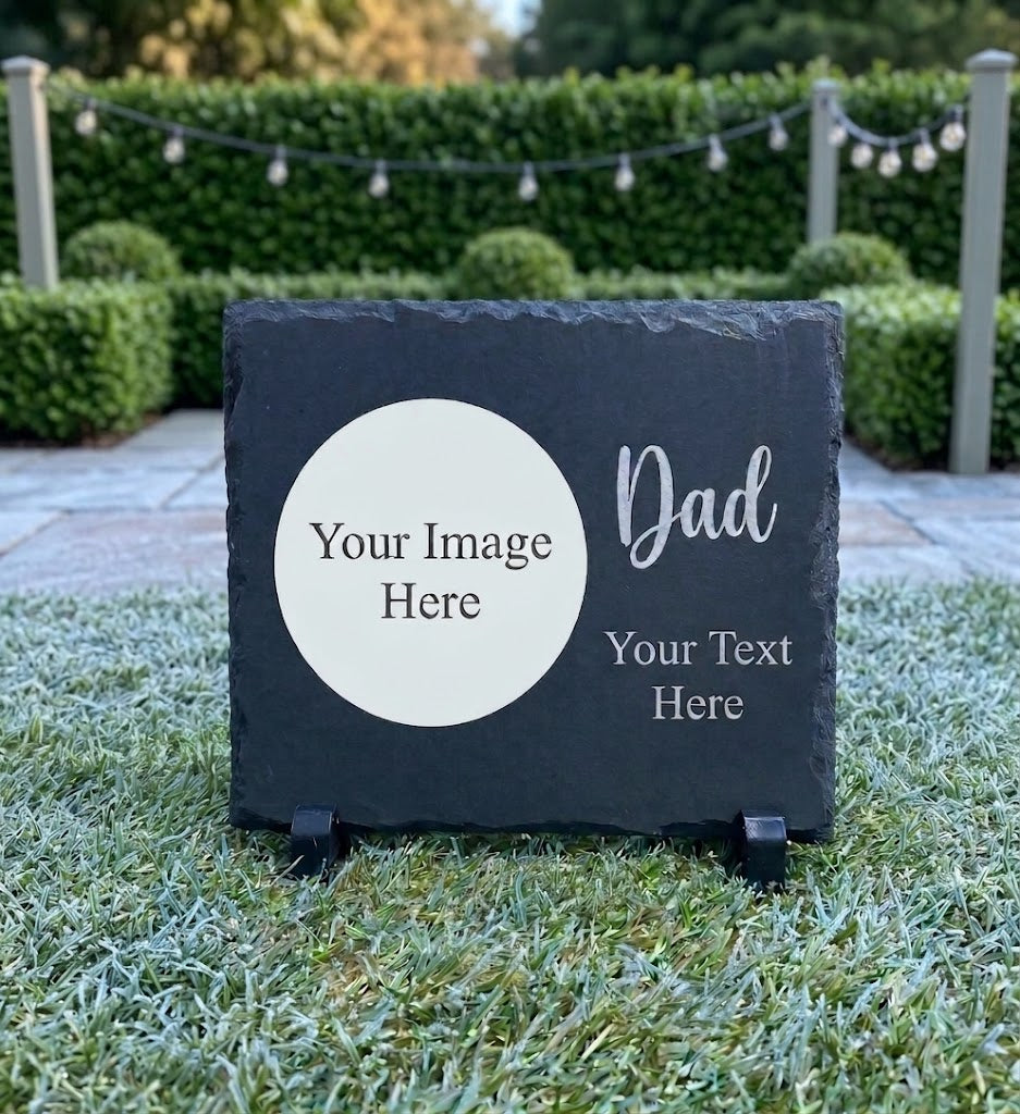 A personalized dark gray slate sign on a small black stand, placed outdoors on grass in front of a hedge. The sign has a white oval placeholder area reading 'Your Image Here' and white text reading 'Dad' and 'Your Text Here'.