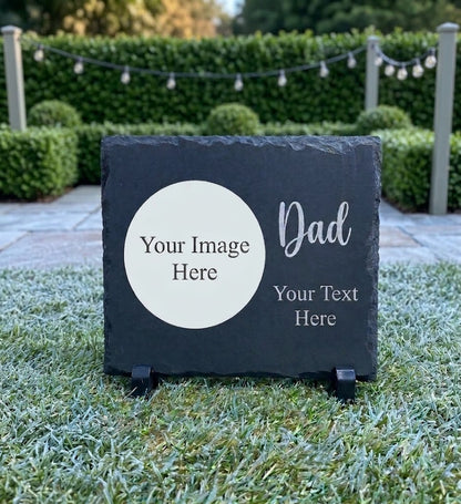 A personalized dark gray slate sign on a small black stand, placed outdoors on grass in front of a hedge. The sign has a white oval placeholder area reading 'Your Image Here' and white text reading 'Dad' and 'Your Text Here'.