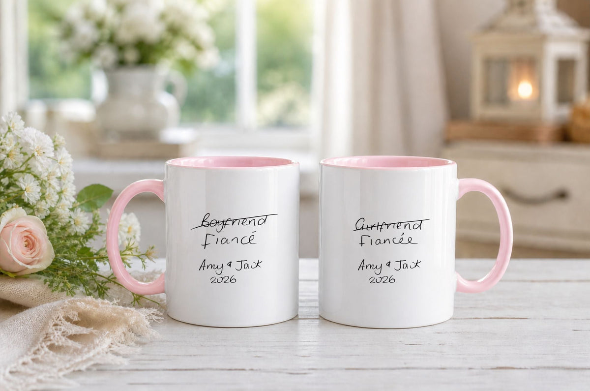 Two white mugs with pink handles on a table with flowers and a blurred background. featuring real handwriting