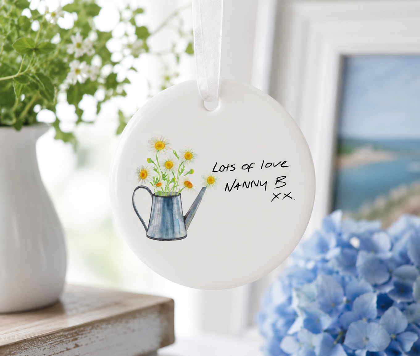 Decorative hanging plate with floral design and text, placed on a surface with plants and flowers in the background.