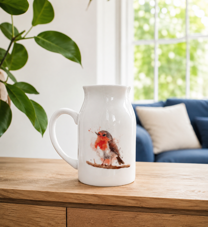White ceramic pitcher with a robin design on a wooden surface, with a blurred indoor background.