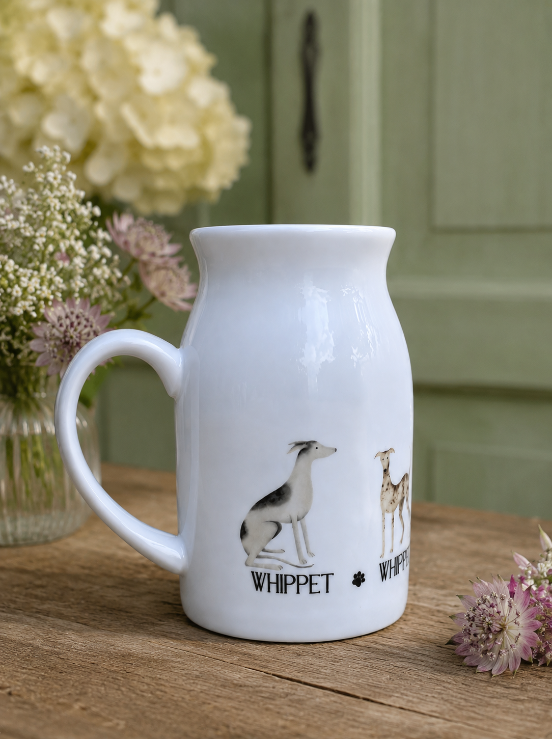 White ceramic jug with dog illustrations on a wooden surface with flowers in the background
