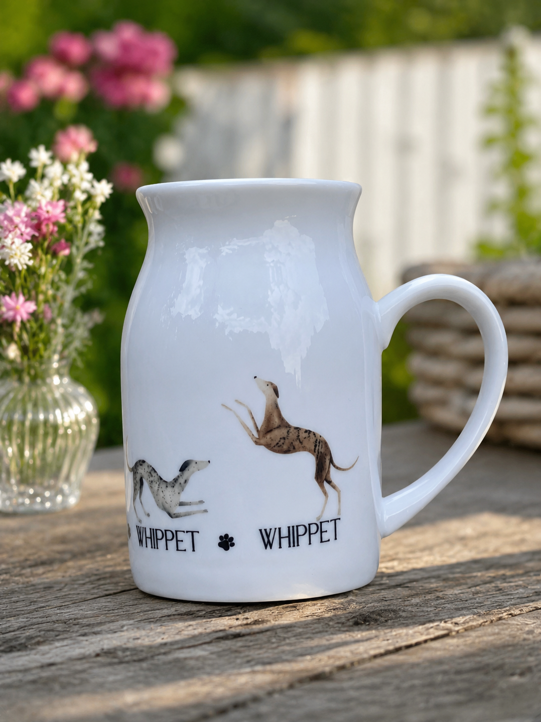 White ceramic mug with whippet dog illustrations on a wooden surface with flowers in the background