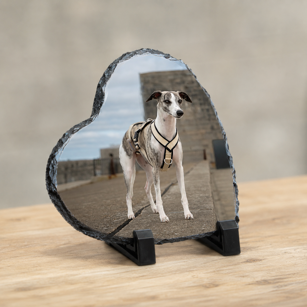 A heart-shaped polished slate plaque on a black stand, featuring a custom photo of a greyhound dog standing on a rooftop. The plaque is displayed on a light wooden table against a neutral beige background.