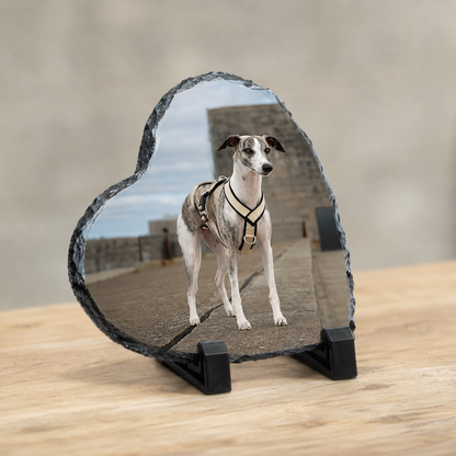 A heart-shaped polished slate plaque on a black stand, featuring a custom photo of a greyhound dog standing on a rooftop. The plaque is displayed on a light wooden table against a neutral beige background.
