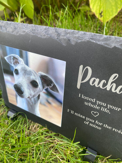 A black memorial garden stone with engraved white text and a photo of a greyhound dog, shown outdoors in green grass.