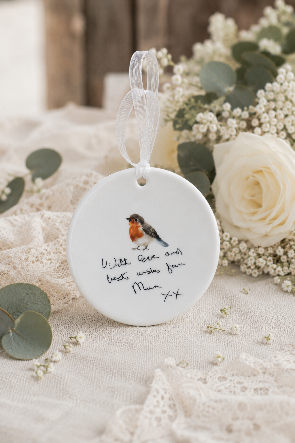 Decorative ornament with a bird illustration and text, placed on a soft fabric background with flowers.